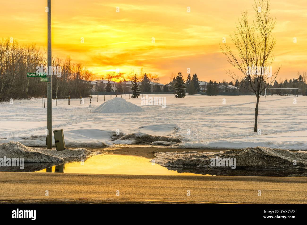 Orange color reflection on puddle from melted snow at the edge of sidewalk at sunset time in early spring season Stock Photo