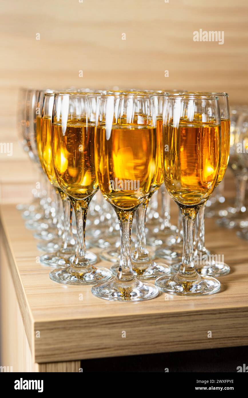 Rows of stemmed glasses filled with sparkling amber apple juice on a wooden counter, reflecting light beautifully. Stock Photo