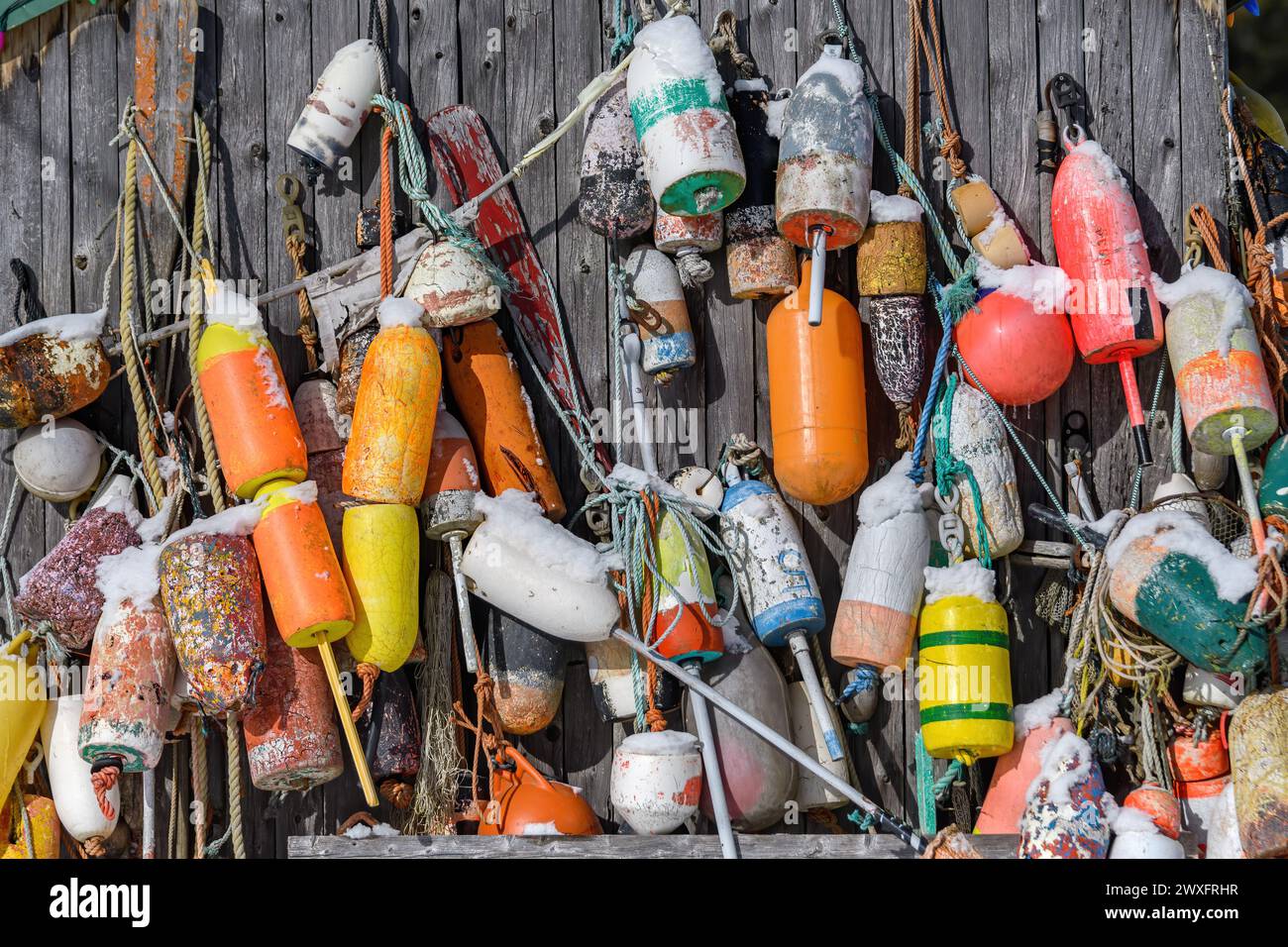 Many fishing buoys hanging from the side of a faded wooden building. These are the type of buoy used by commercial fishermen. Stock Photo