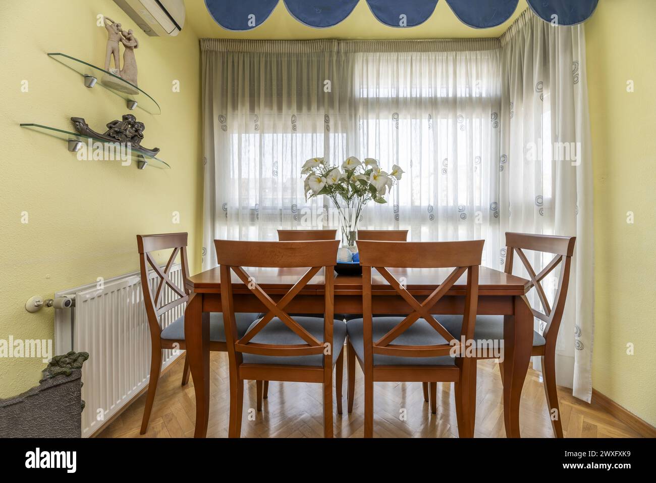cherry wood dining table with matching blue upholstered chairs and a large window with white curtains Stock Photo