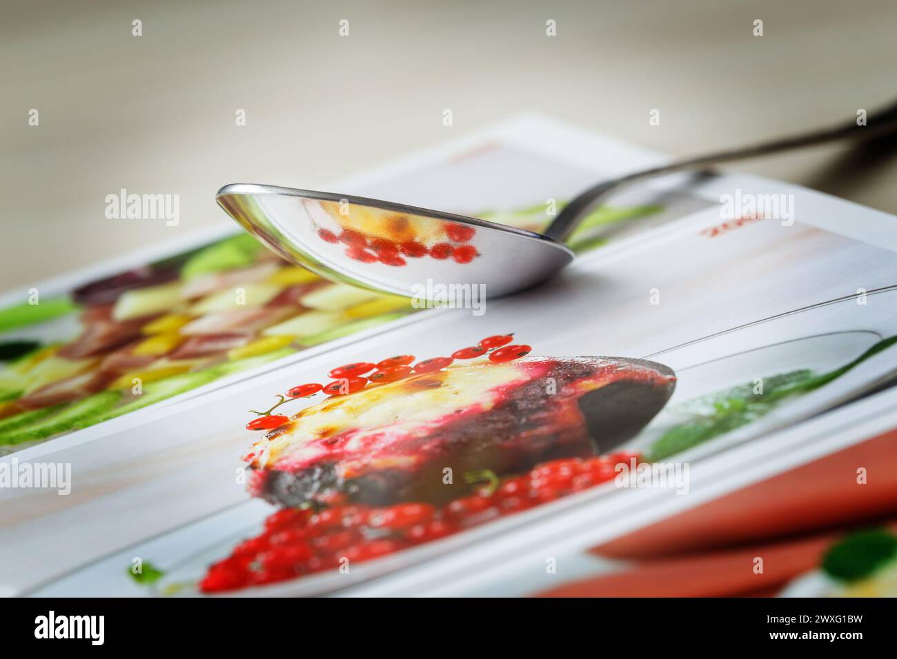 The spoon lying on the cookbook reflects a picture from a recipe with red berries. Stock Photo