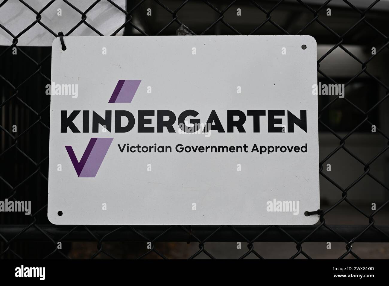 White Kindergarten Victorian Government Approved sign, attached to a black chain link fence, outside one of the state's early education centres Stock Photo