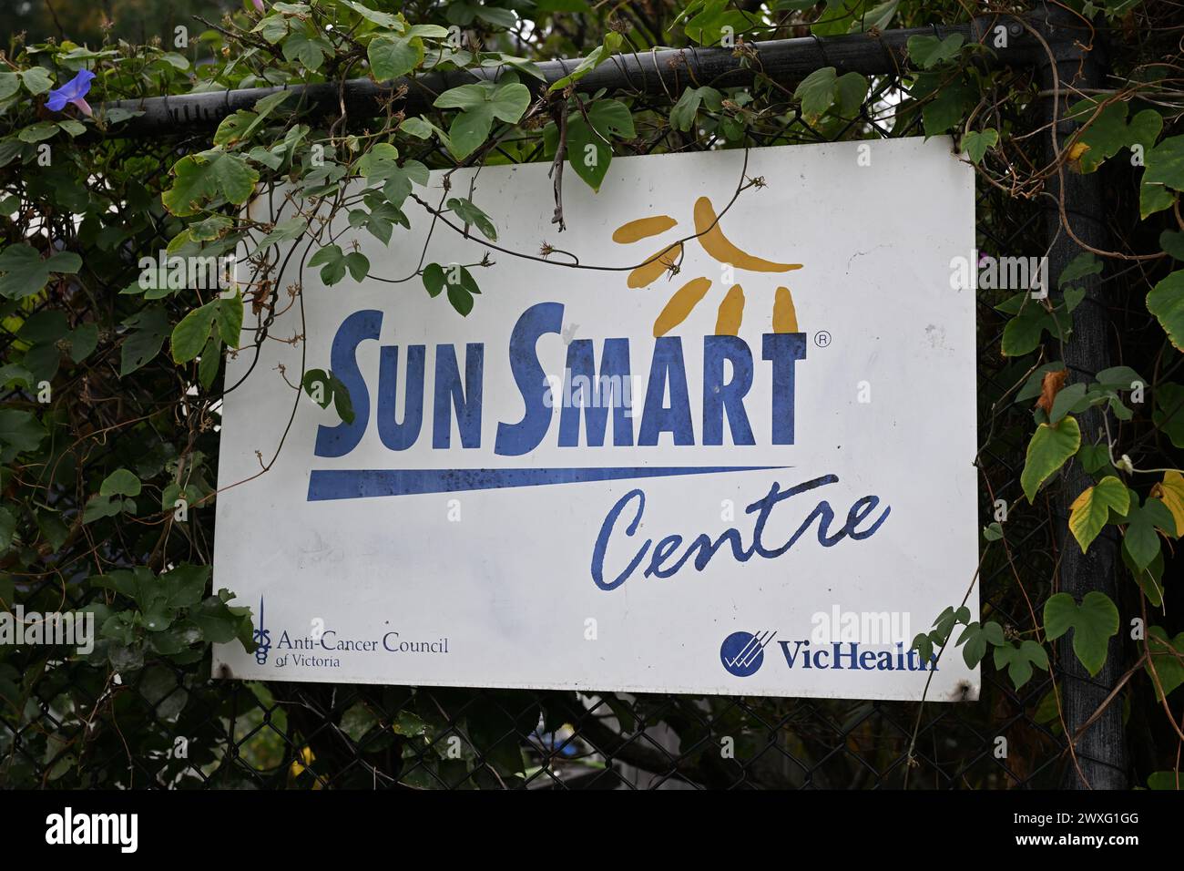 Partially obscured white Sun Smart Centre sign from the Anti-Cancer Council of Victoria and VicHealth, attached to a black chain link fence Stock Photo