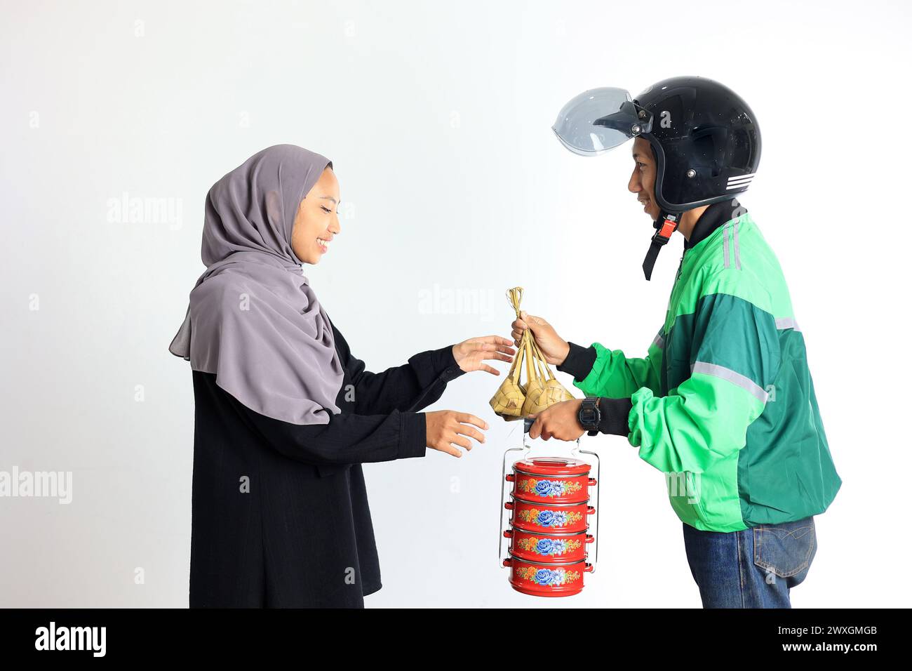 Asian Commercial Online Taxi Driver Delivery Ketupat and Side Dish on Traditional Indonesian Lunchbox Rantang to Femlae Customer for Eid Al Fitr or Le Stock Photo