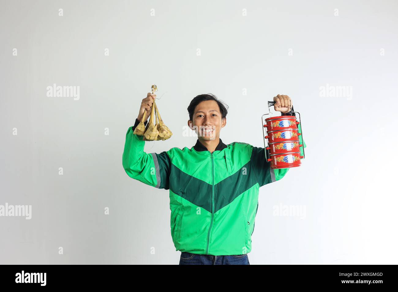 Asian Male Online Driver Delivering Ketupat and Side Dish on Red Stacked LUnchbox or Rantang. Rantangan, Sharing Food during Ramadan or Lebaran in Ind Stock Photo