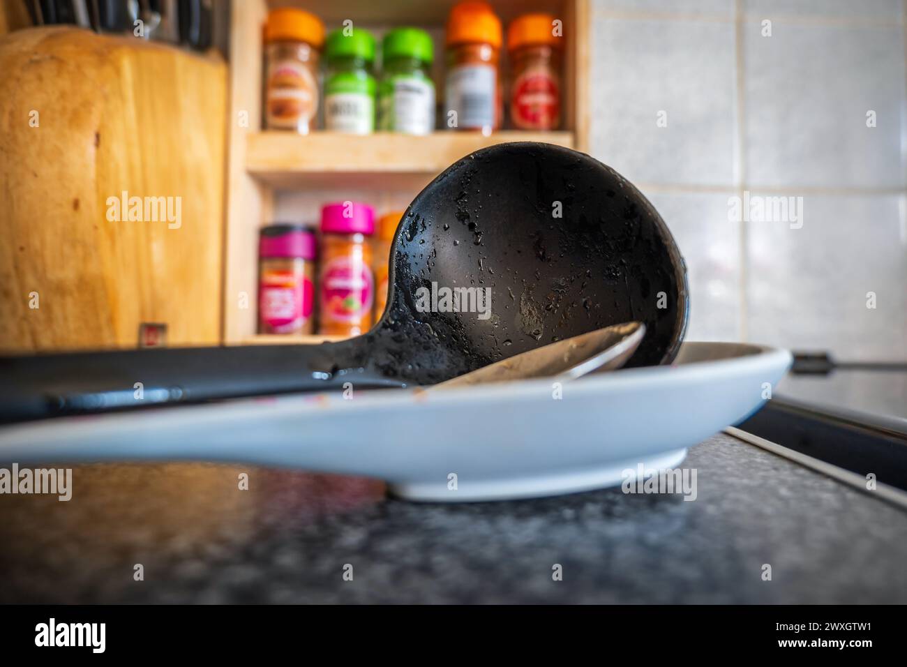 Soup leftovers on black plastic ladle on kitchen tabletop. Stock Photo