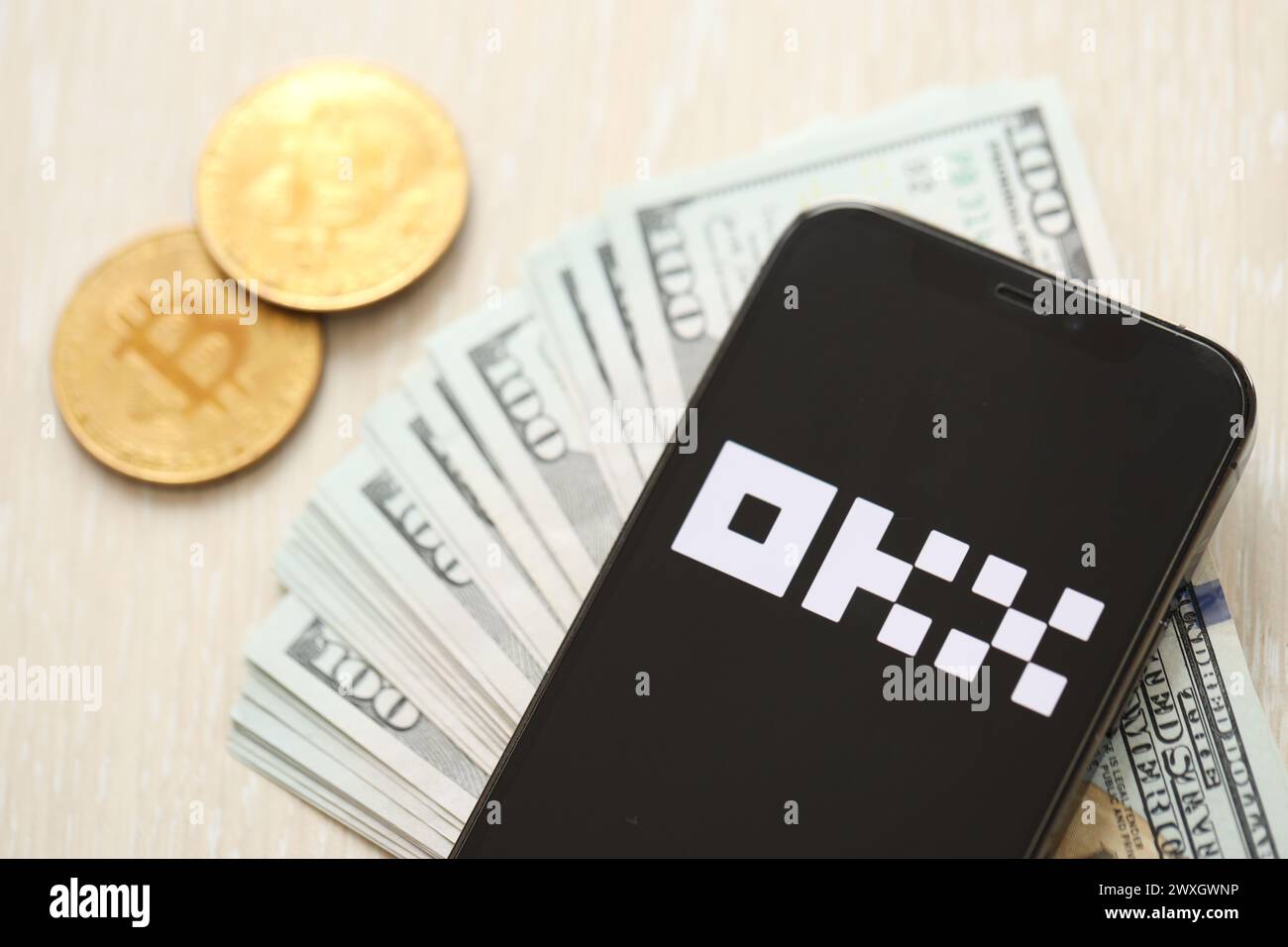 KYIV, UKRAINE - MARCH 15, 2024 OKX logo on iPhone display screen with dollars and bitcoins on table. Cryptocurrency exchange portal Stock Photo
