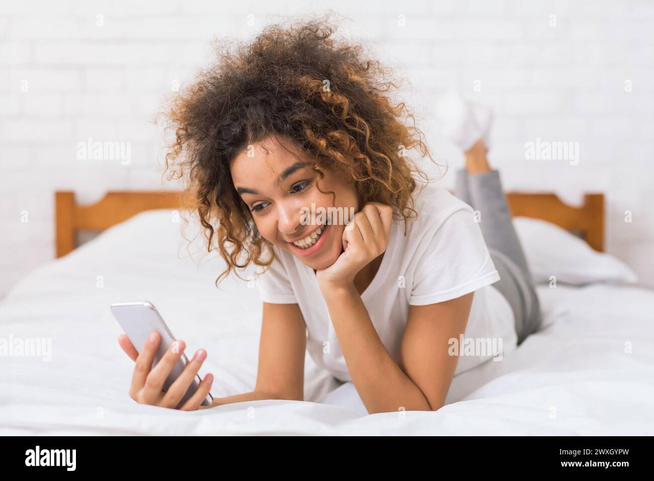 Curly-haired woman looking at phone in bed Stock Photo