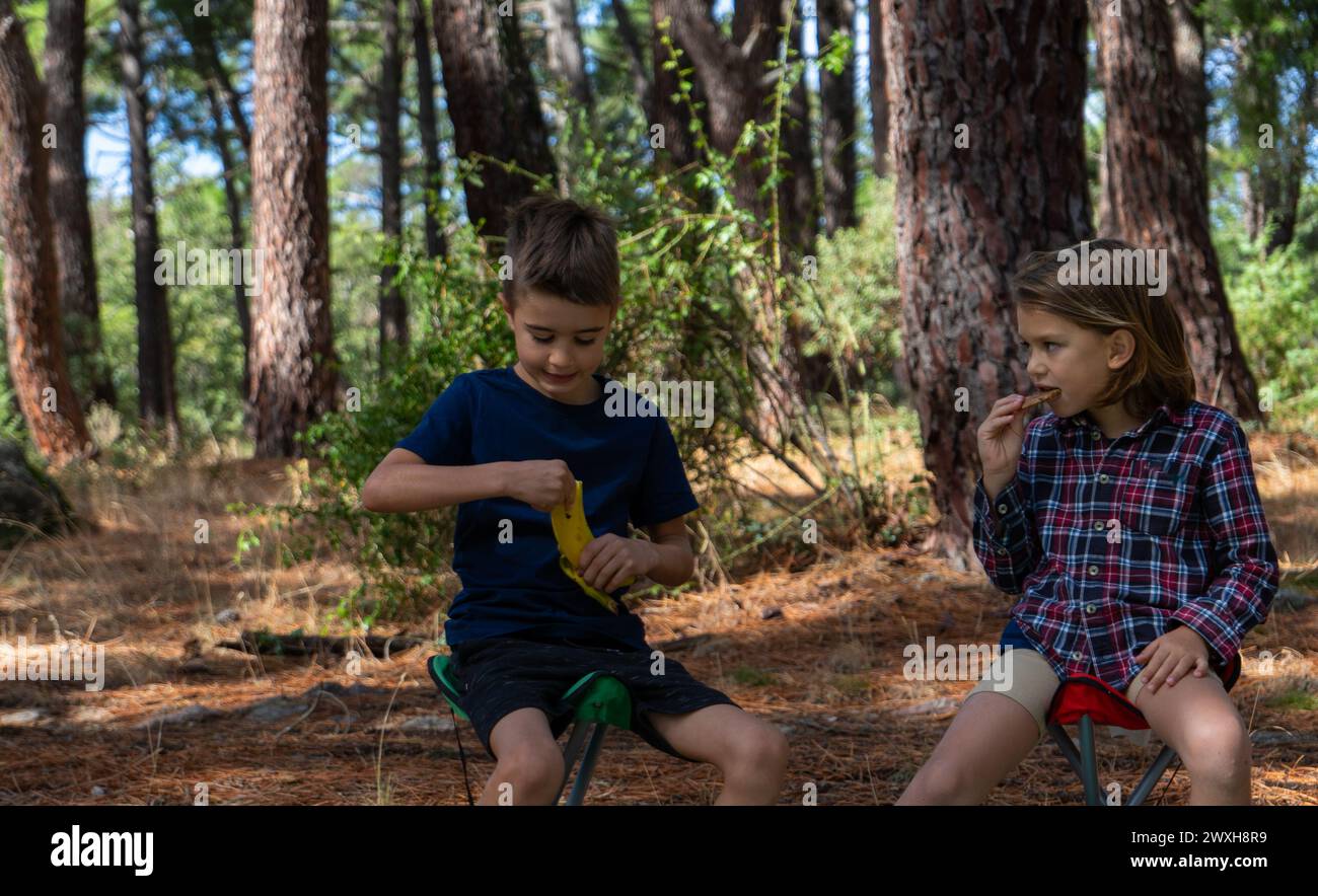 Two children eating in the forest, one a cookie and the other a banana Stock Photo