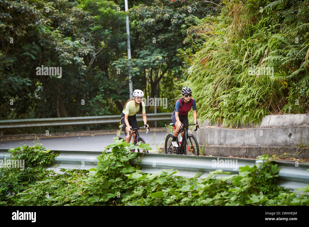 two young asian women cyclists riding bike on rural road Stock Photo