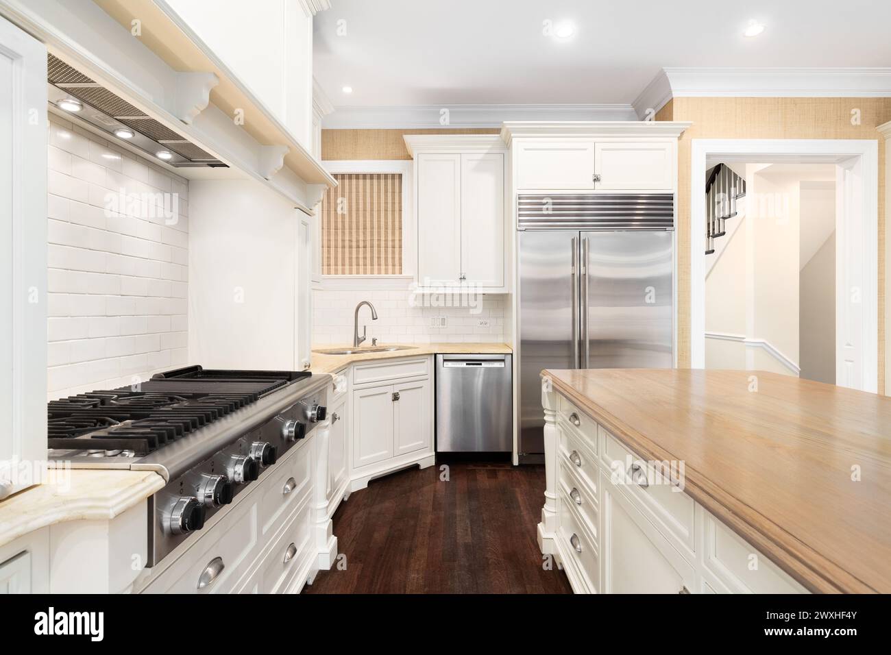 A kitchen detail with stainless steel appliances, a large range hood over a stove top, and white cabinets. No brands or labels. Stock Photo