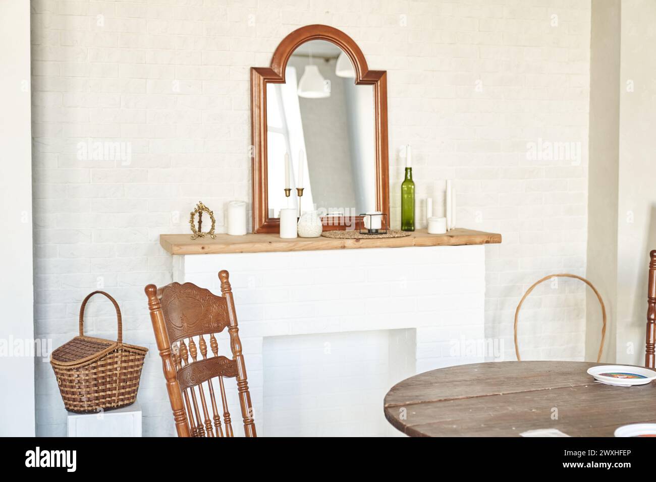 Interior design of room with fireplace, vintage mirrow, candles, wicker basket, wooden chair, table, white brick wall. Background with copy space, empty. Template, mockup for design, poster, art. Stock Photo