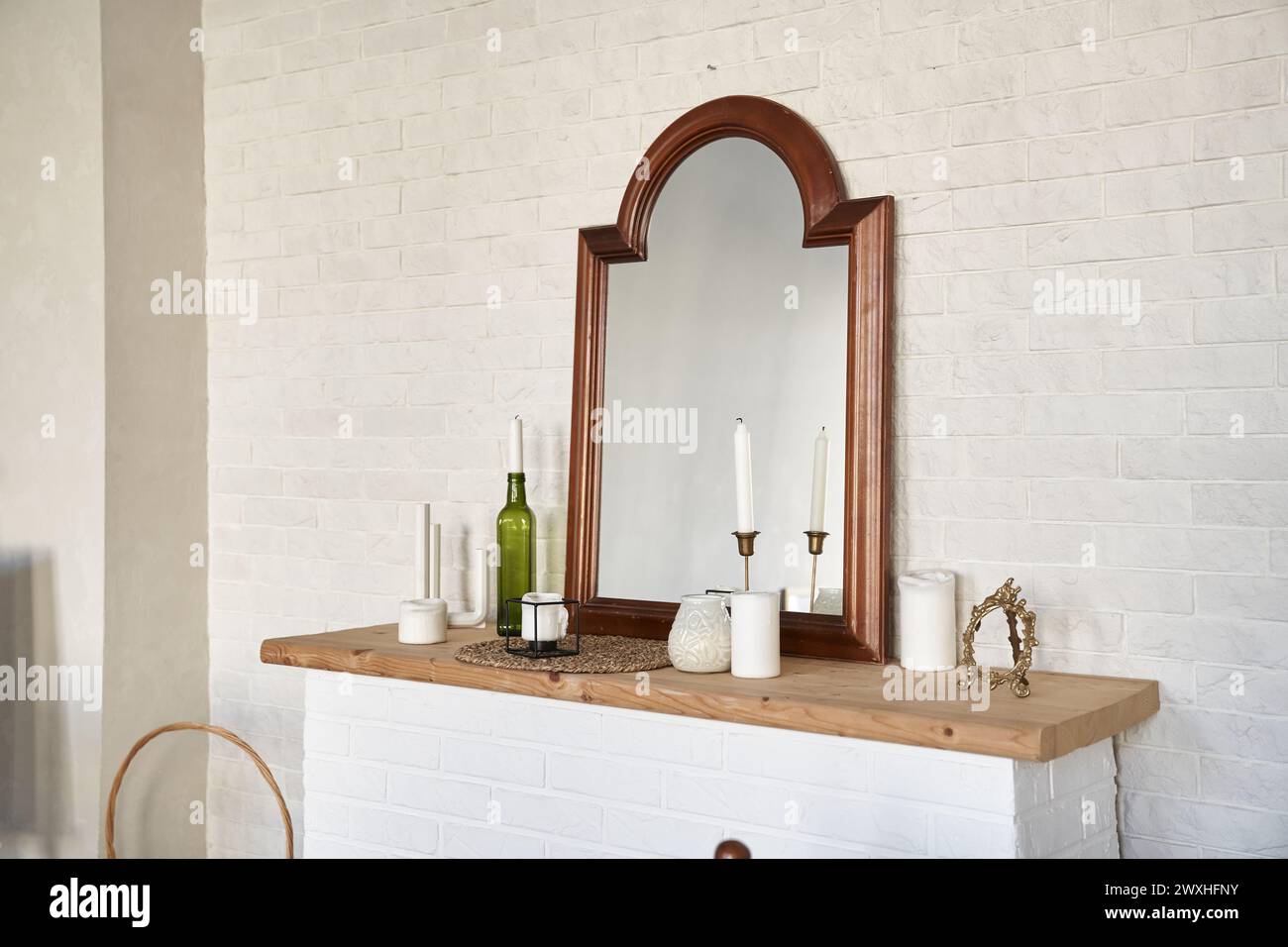 Interior design of bright room with vintage mirrow standing on top of fireplace, candles, white brick wall. Background with copy space, empty. Template, mockup for design, poster, art, object. Stock Photo