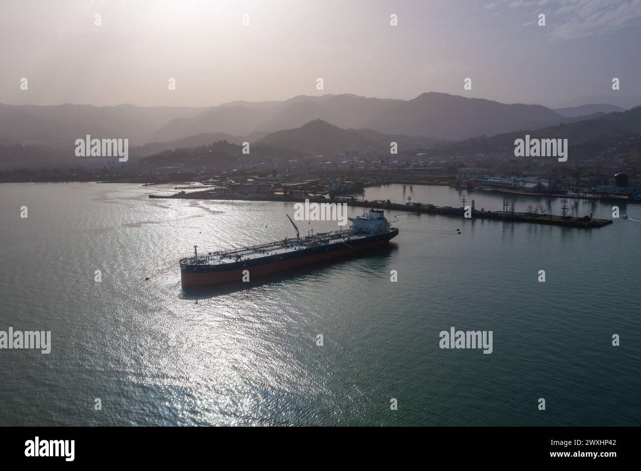 Tanker moored at oil terminal, intricate part of global petro resource trade, aerial view from drone. Key hub in industry logistics and distribution. Essential in the chain of energy supply and commerce. Stock Photo