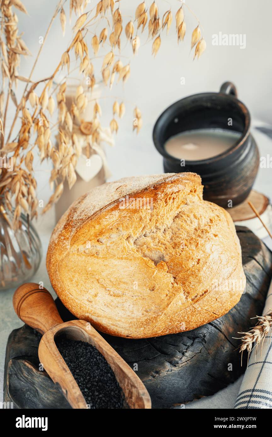 Round white bread. Close-up of homemade white bread with black salt in wooden scoop and milk on light marble background. Stock Photo