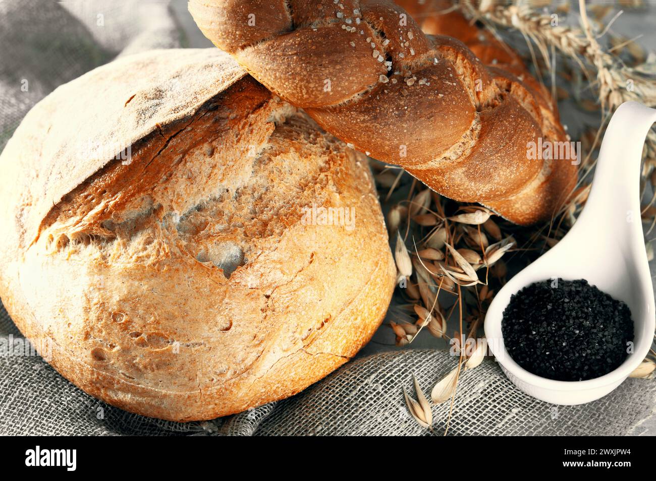 Round white bread. Close-up of homemade white bread with black salt in a white porcelain salt cellar. Close-up. Stock Photo