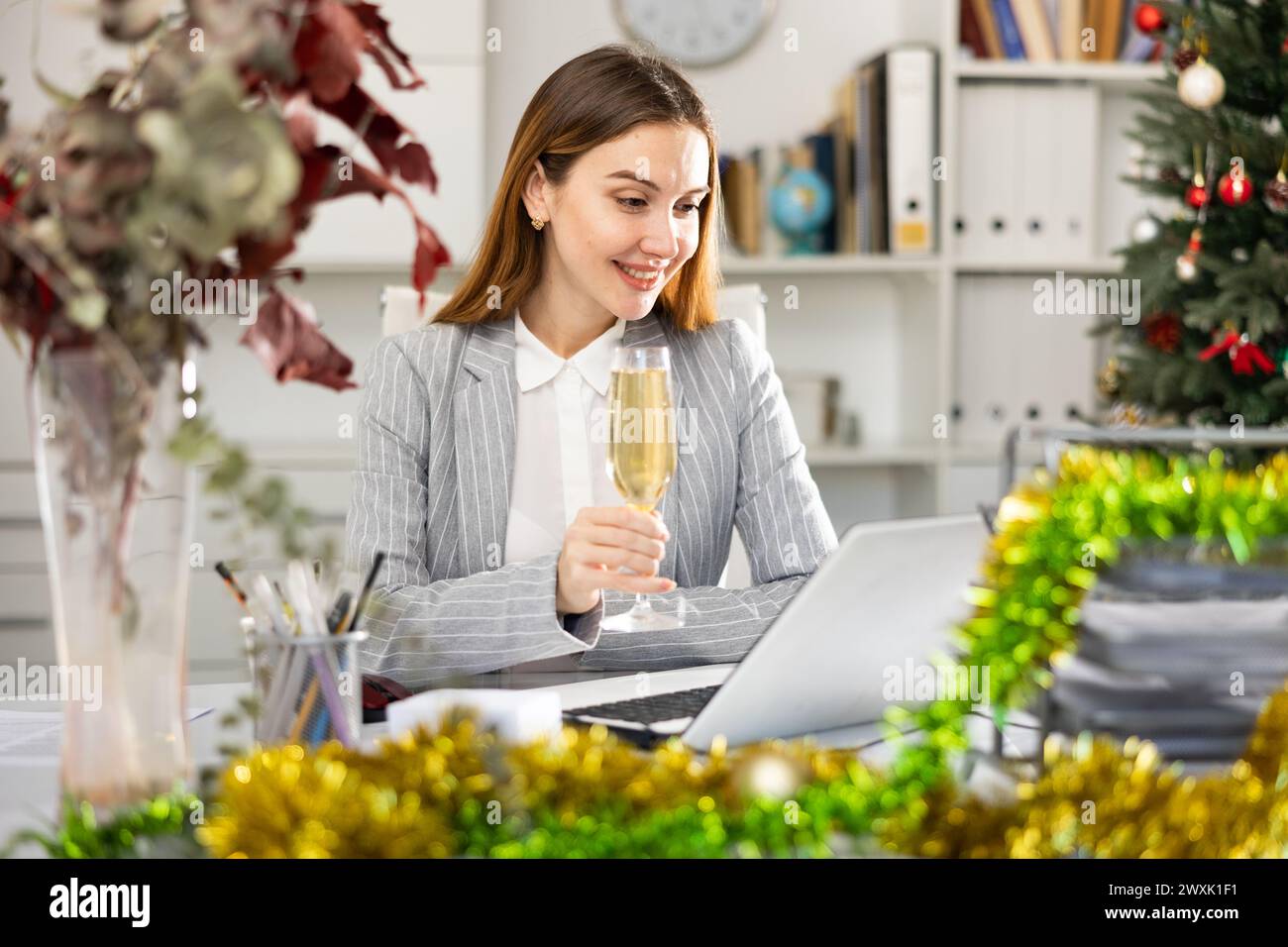 Business woman with a glass of champagne congratulates Merry Christmas on the Internet in office Stock Photo