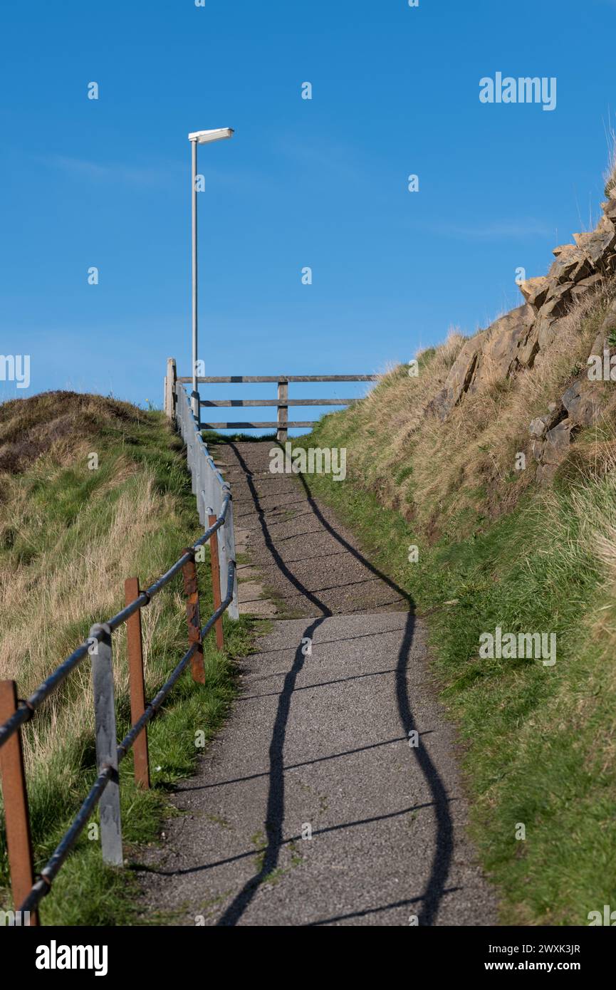 31 March 2024. Cullen,Moray,Scotland. This is a footpath leading from the harbour area at Cullen on a sunny day, the shadows of the handrail guide the Stock Photo