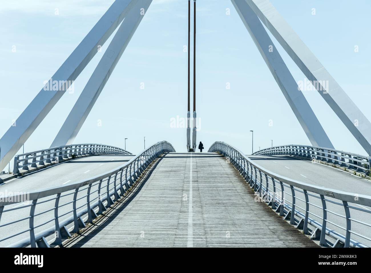 Metal structure of a small bridge with hanging metal structure, walkways and wooden floors for pedestrians on a nice sunny day with a lone pedestrian Stock Photo