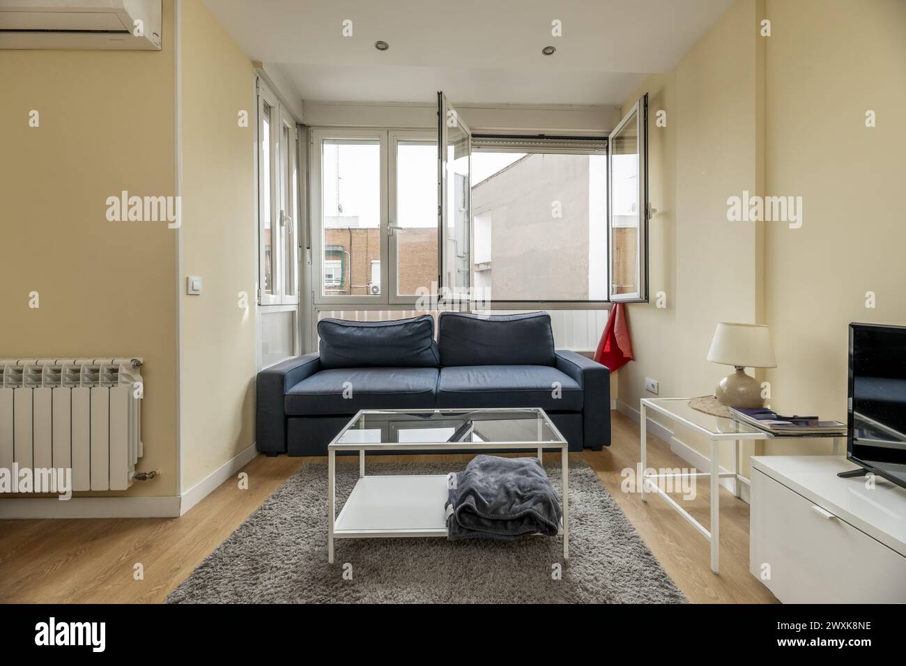 a sofa under a window, air conditioning in the room, a coffee table with a glass top Stock Photo