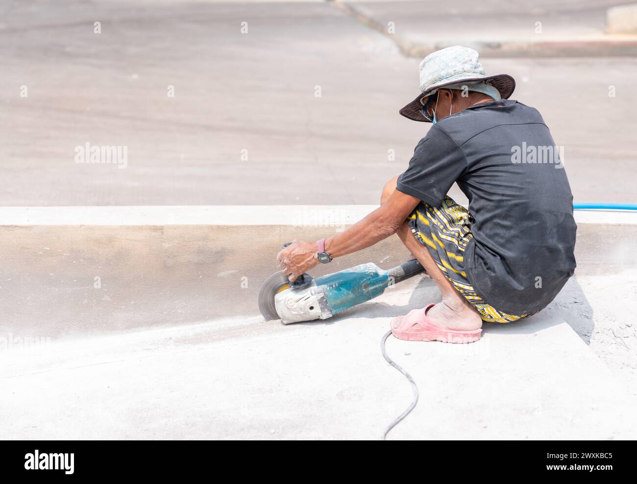Worker cutting the concrete slab with electric circular saw and dust fly arround without personal protective equipment in Construction site. Stock Photo