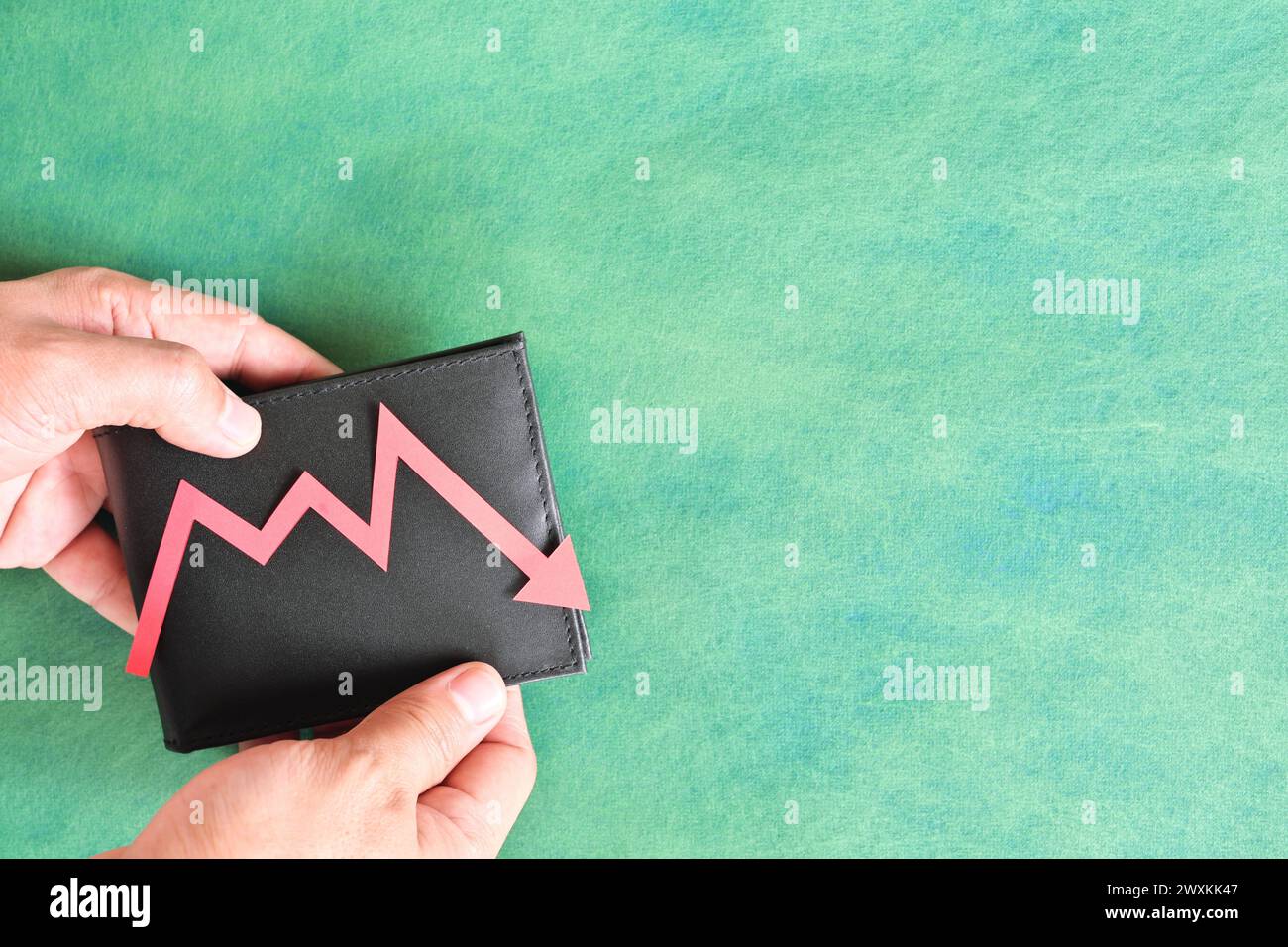 Male hand holding a wallet with red downward arrow. Money value currency depreciation and inflation concept. Stock Photo