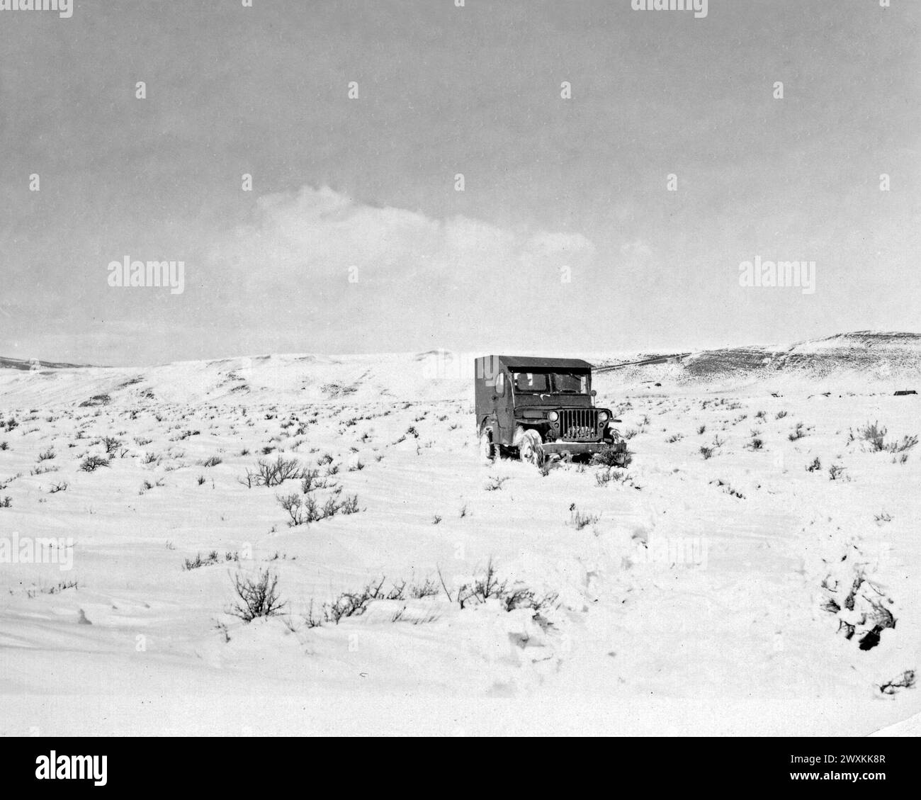 A jeep drives across a snowy field in rural Wyoming ca. 1930s or 1940s Stock Photo