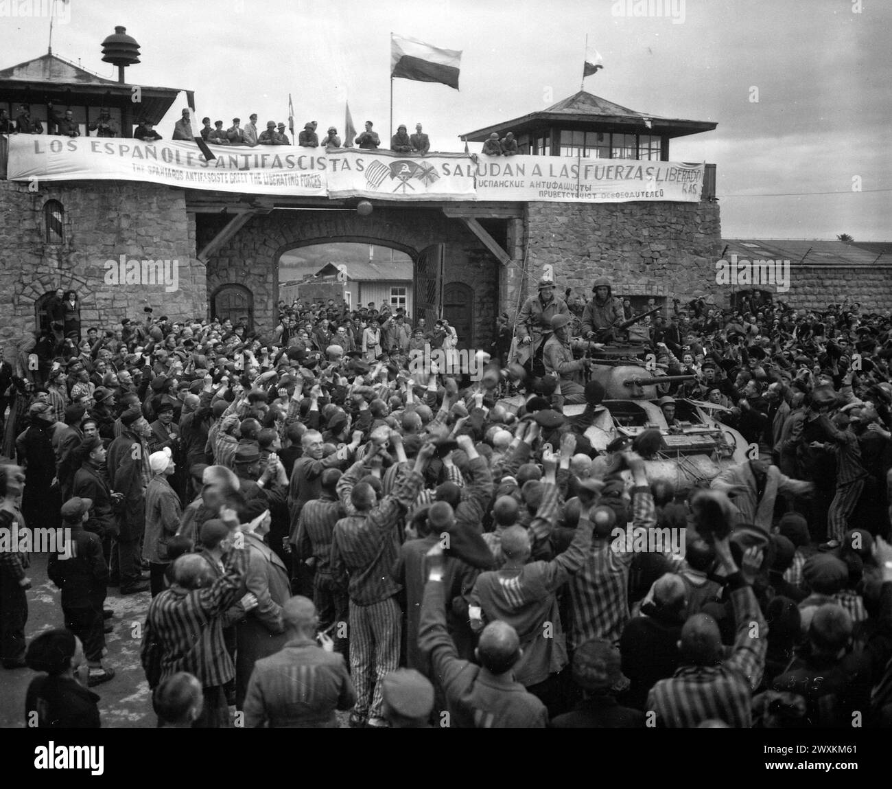 Liberated prisoners in the Mauthausen concentration camp near Linz, Austria, give rousing welcome to Cavalrymen of the 11th Armored Division. The banner across the wall was made by Spanish Loyalist prisoners ca. May 6, 1945 Stock Photo