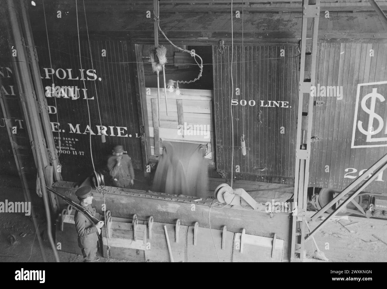 Pillsbury Flour Mills, Minneapolis, MN - Unloading wheat using power-operated shovels, worker and soldier in the image ca. 1917 Stock Photo