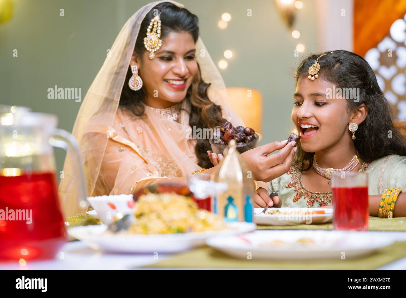 Happy indian mother feeding dates to daughter during ramadan iftar