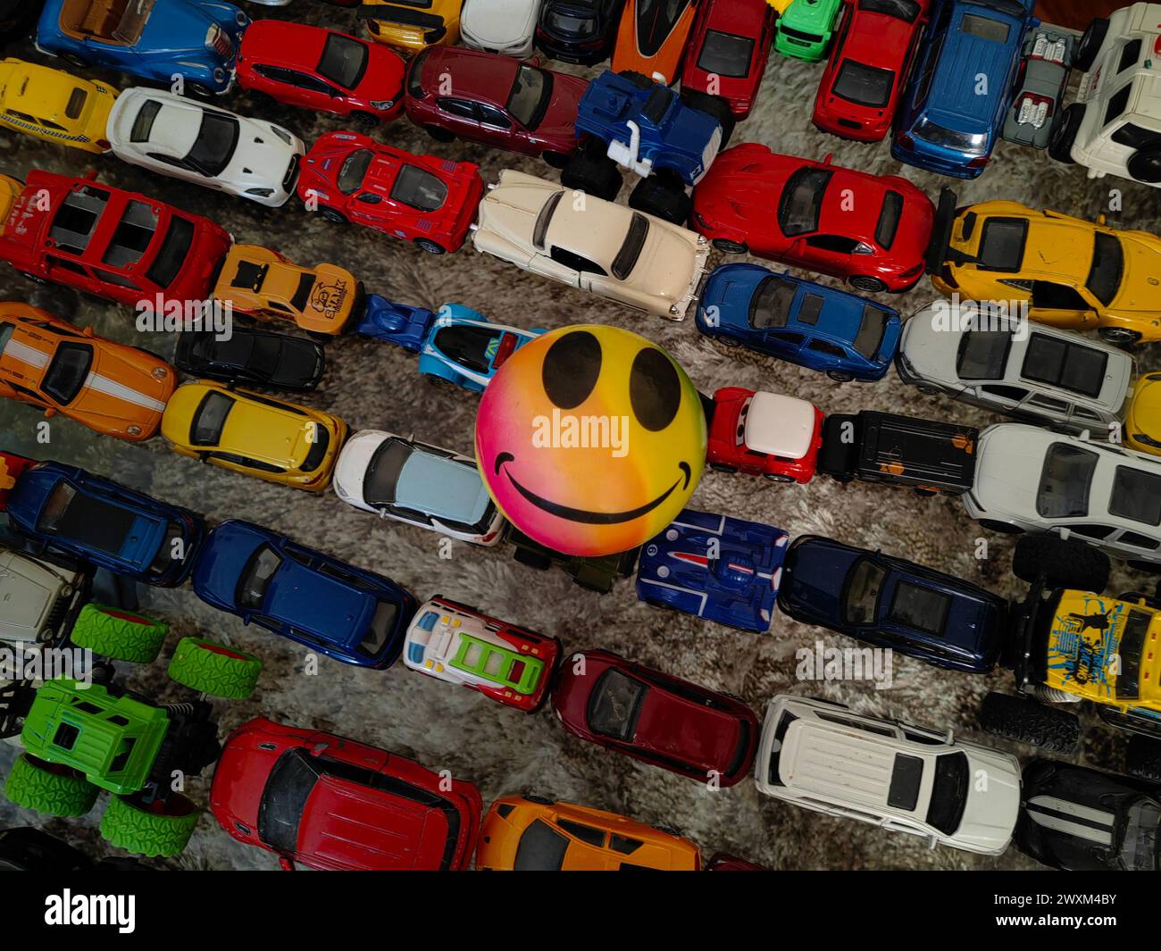 Stuck in traffic jam, concept. Child's play. Always be happy, and smile. Don't worry. Part of growth.  Round ball with smiley emotion. Many toy cars. Stock Photo