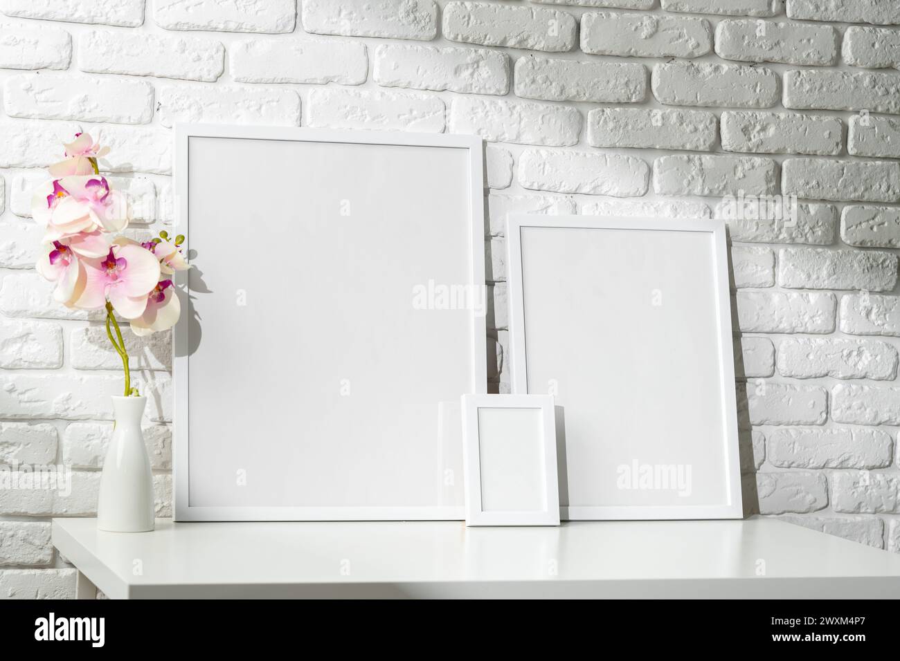 Three Blank Photo Frames on a White Table Against a Brick Wall Background Stock Photo