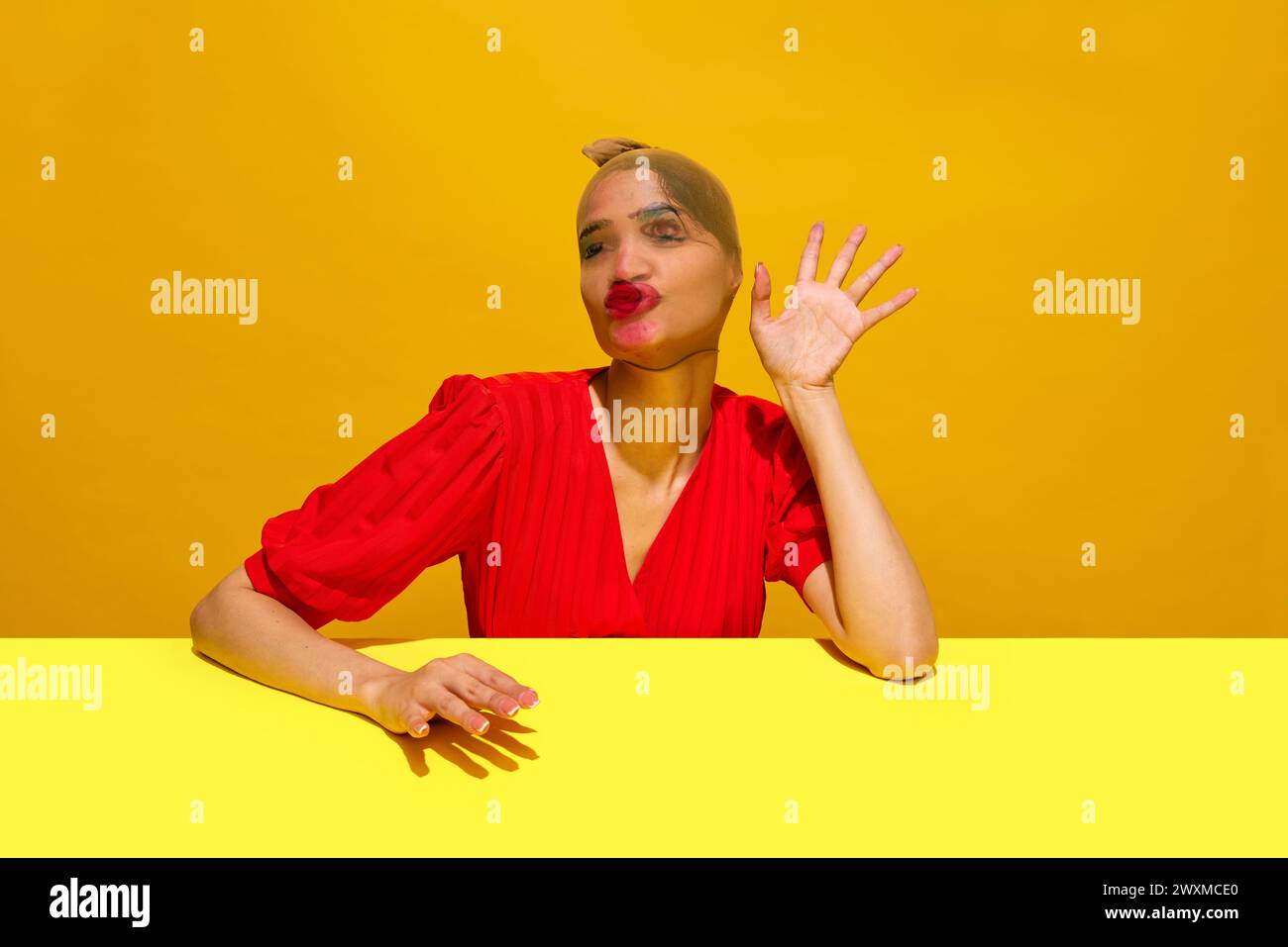 Young woman with stocking over head with smudged lipstick makeup making funny expression against yellow background Stock Photo