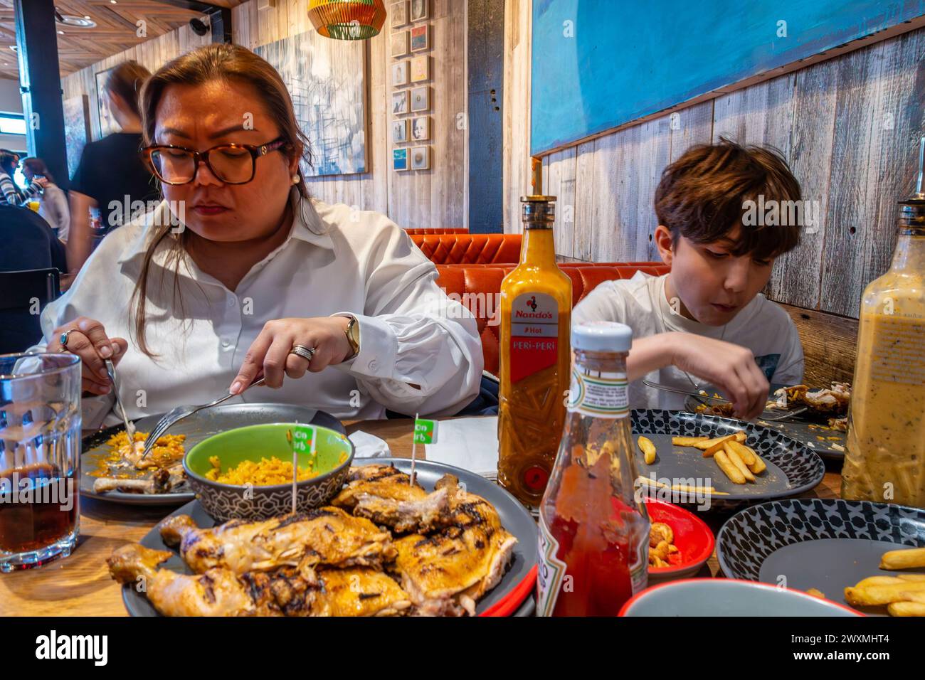 A mother and son eat grilled chicken together at a Nandos restaurant Stock Photo