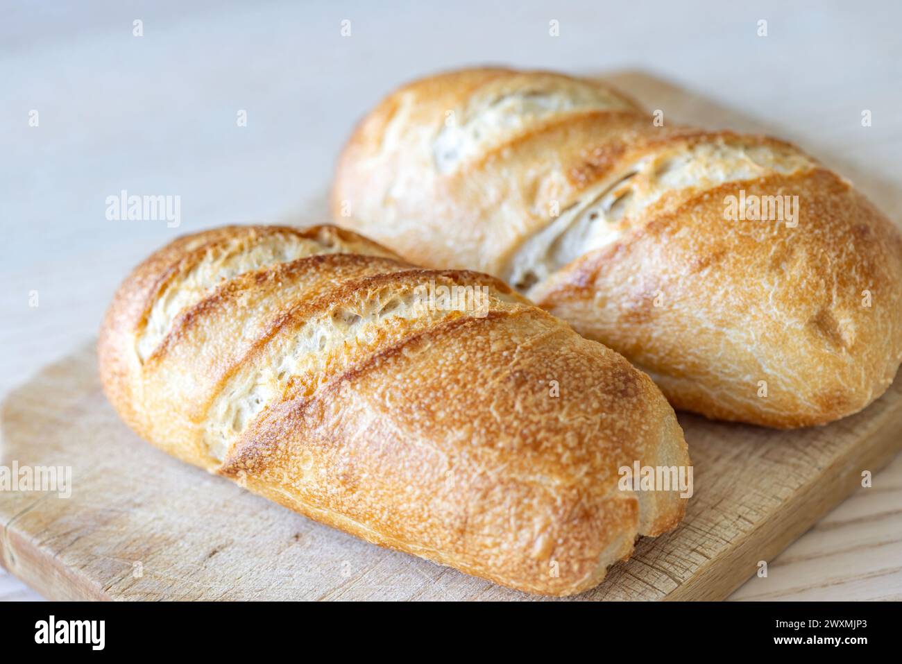 Two crusty golden brown bread loaves on wooden cutting board. Stock Photo