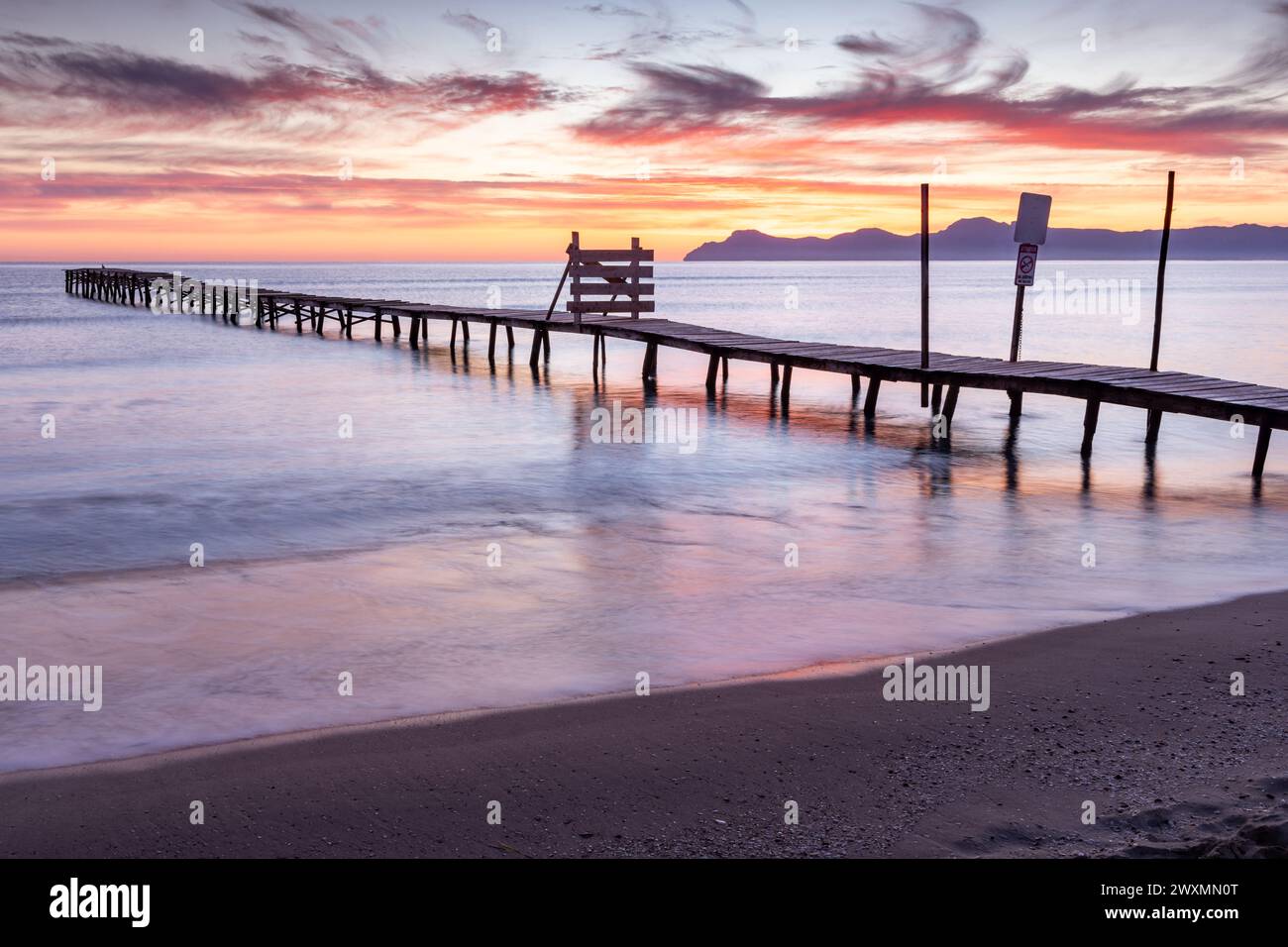 Beautiful sunrise on a beach with old wooden jetty in Platja de Muro, Majorca, Balearic Islands, Spain Stock Photo