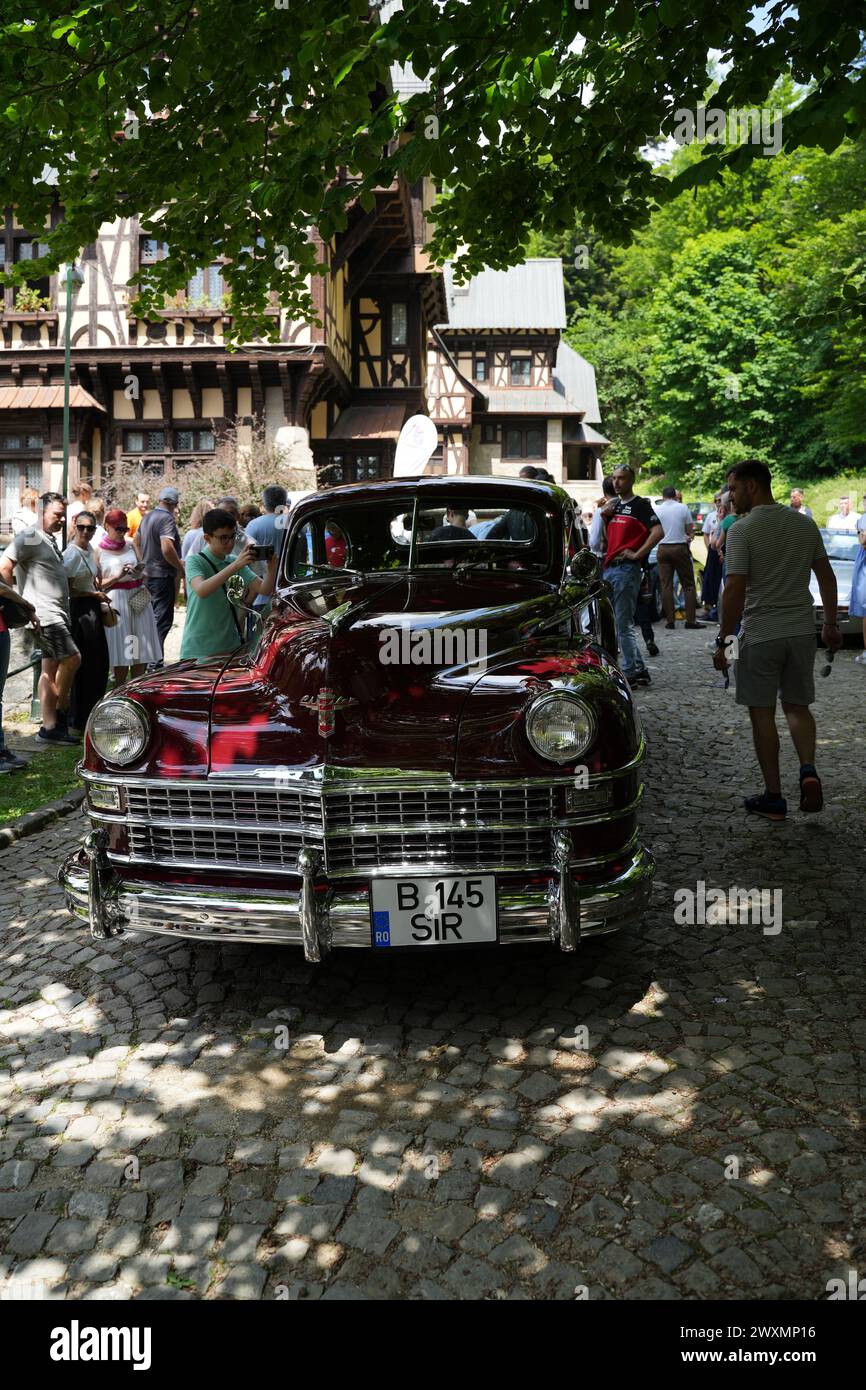 A maroon 1947 Chrysler Windsor Highlander Convertible parked under a tree on a cobblestone road Stock Photo