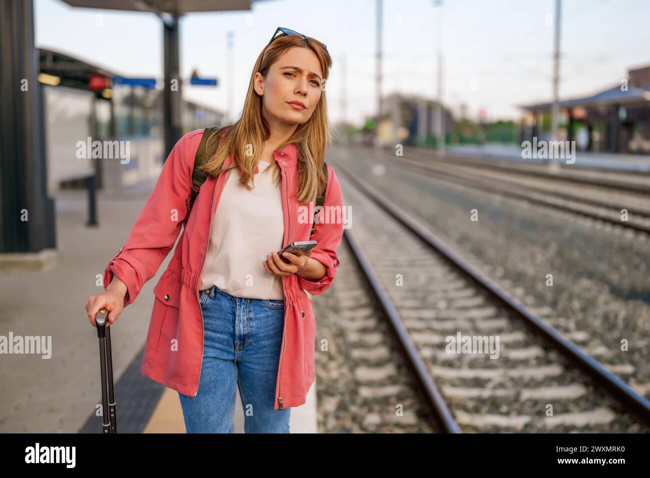 Adult woman is standing at railway station and waiting for arrival of train. Stock Photo