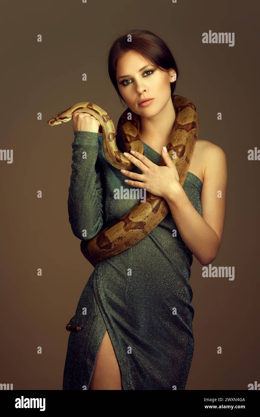 Young woman in glittery green dress with makeup, posing with snake against  brown studio background Stock Photo - Alamy