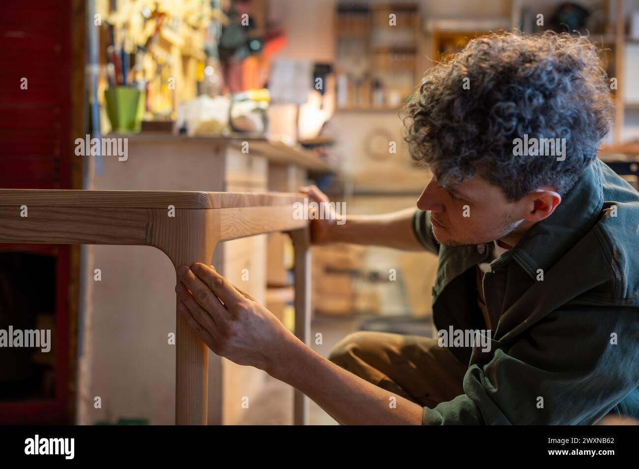 Carpentry workshop, male craftsman working. Professional artisan smiles, checking wooden table Stock Photo