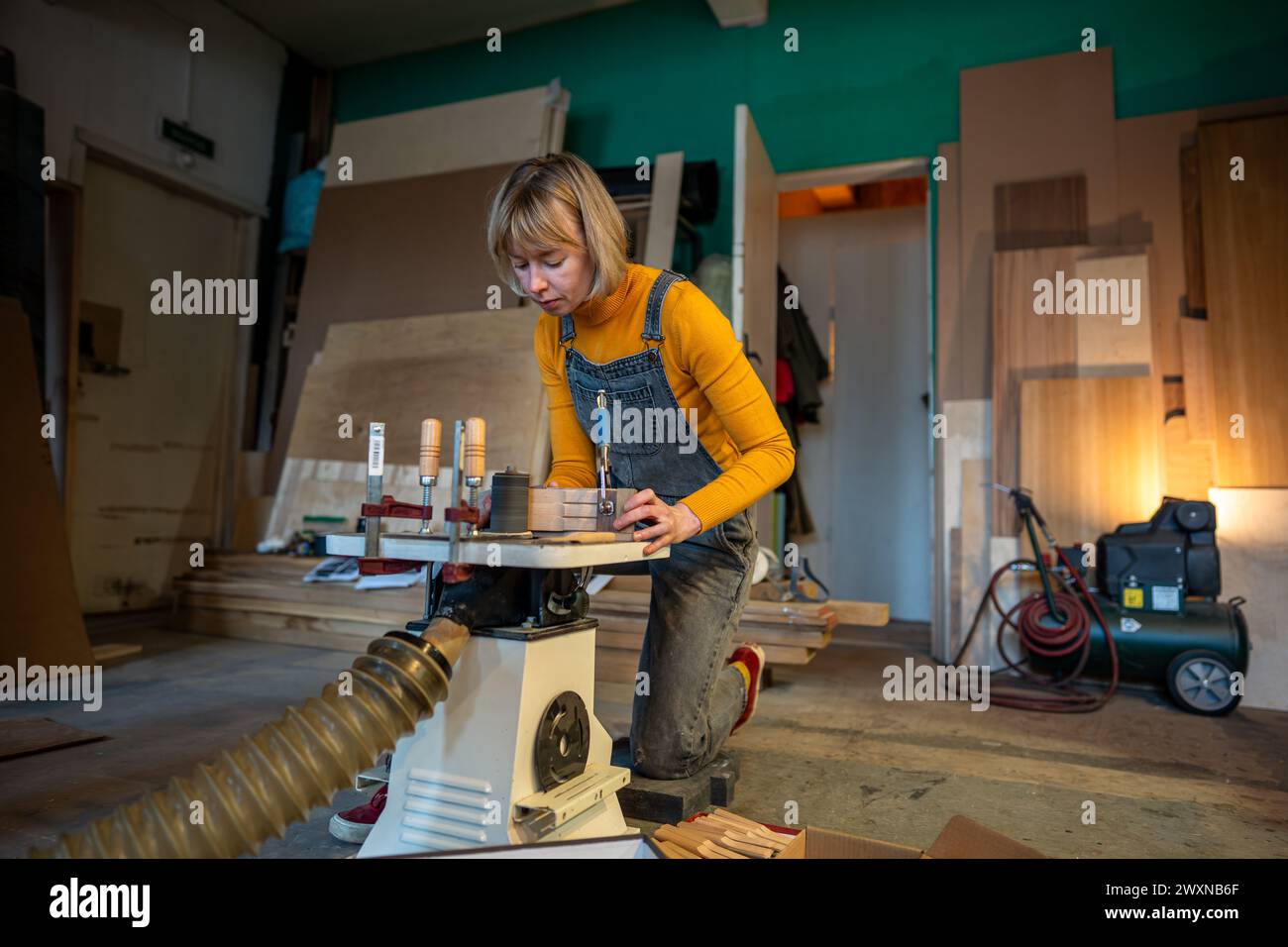 Pedant woman joiner works in joinery workshop, sanding, turning wooden knife blanks on lathe Stock Photo