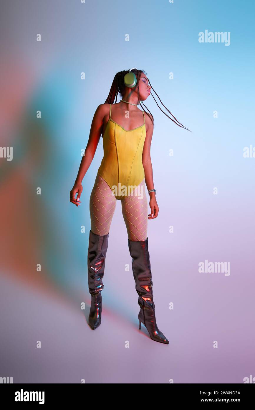 young african american woman in headphones posing in yellow bodysuit and over knee boots, shake head Stock Photo
