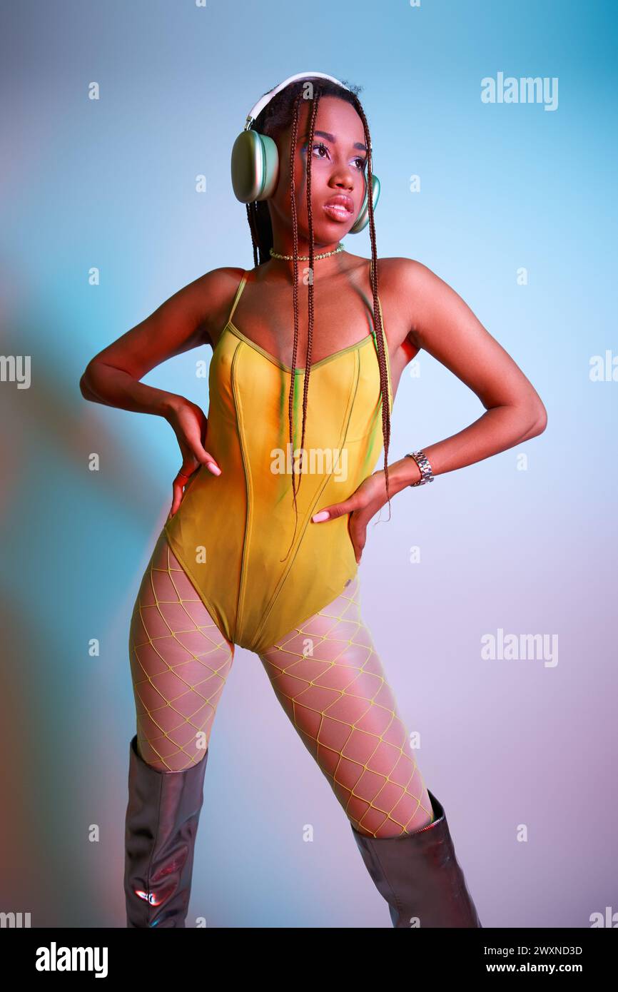 young african american woman in headphones posing in yellow bodysuit and over knee boots in studio Stock Photo
