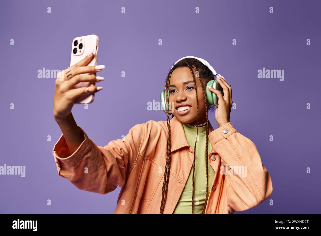 Cheerful african american woman in 20s taking selfie with her headphones on lilac backdrop Stock Photo