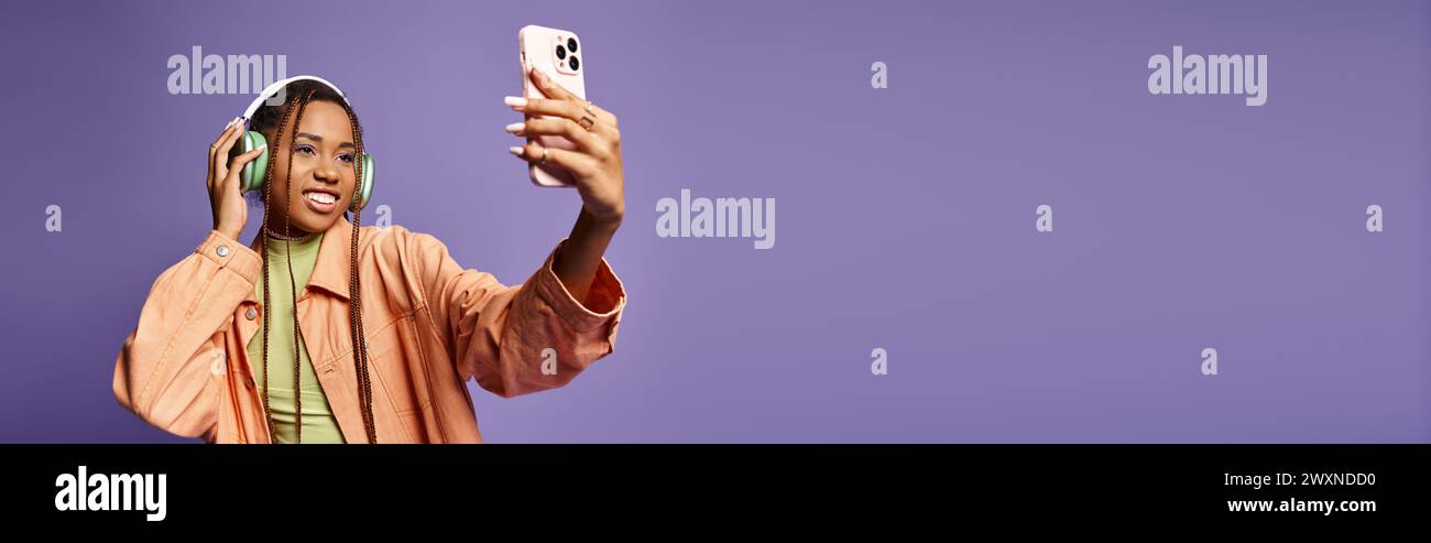 Cheerful african american woman in 20s taking selfie with her headphones on lilac backdrop, banner Stock Photo