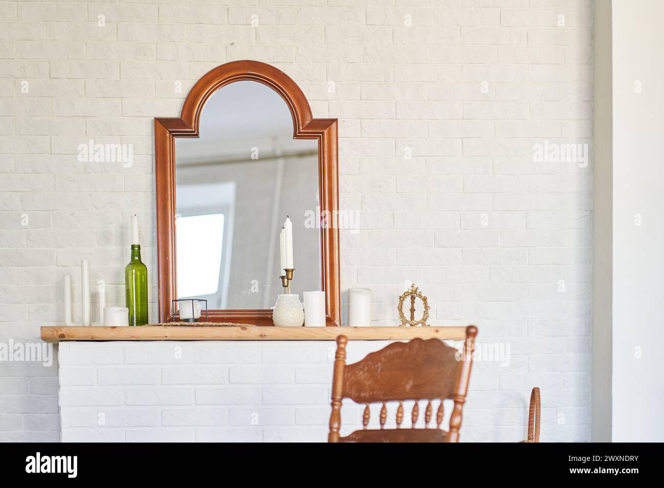 Interior design of room with vintage mirrow, fireplace, candles, bottle, chair, white brick wall. Background with copy space, empty. Template, mock up for your design, poster, art, picture. Stock Photo