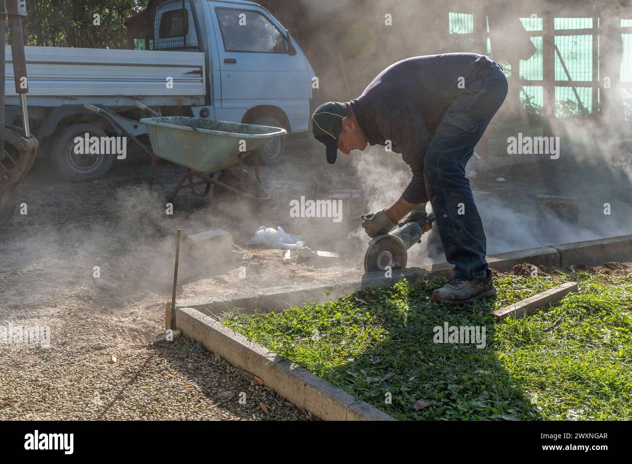 A worker builds a curb using various tools including an angle grinder Stock Photo