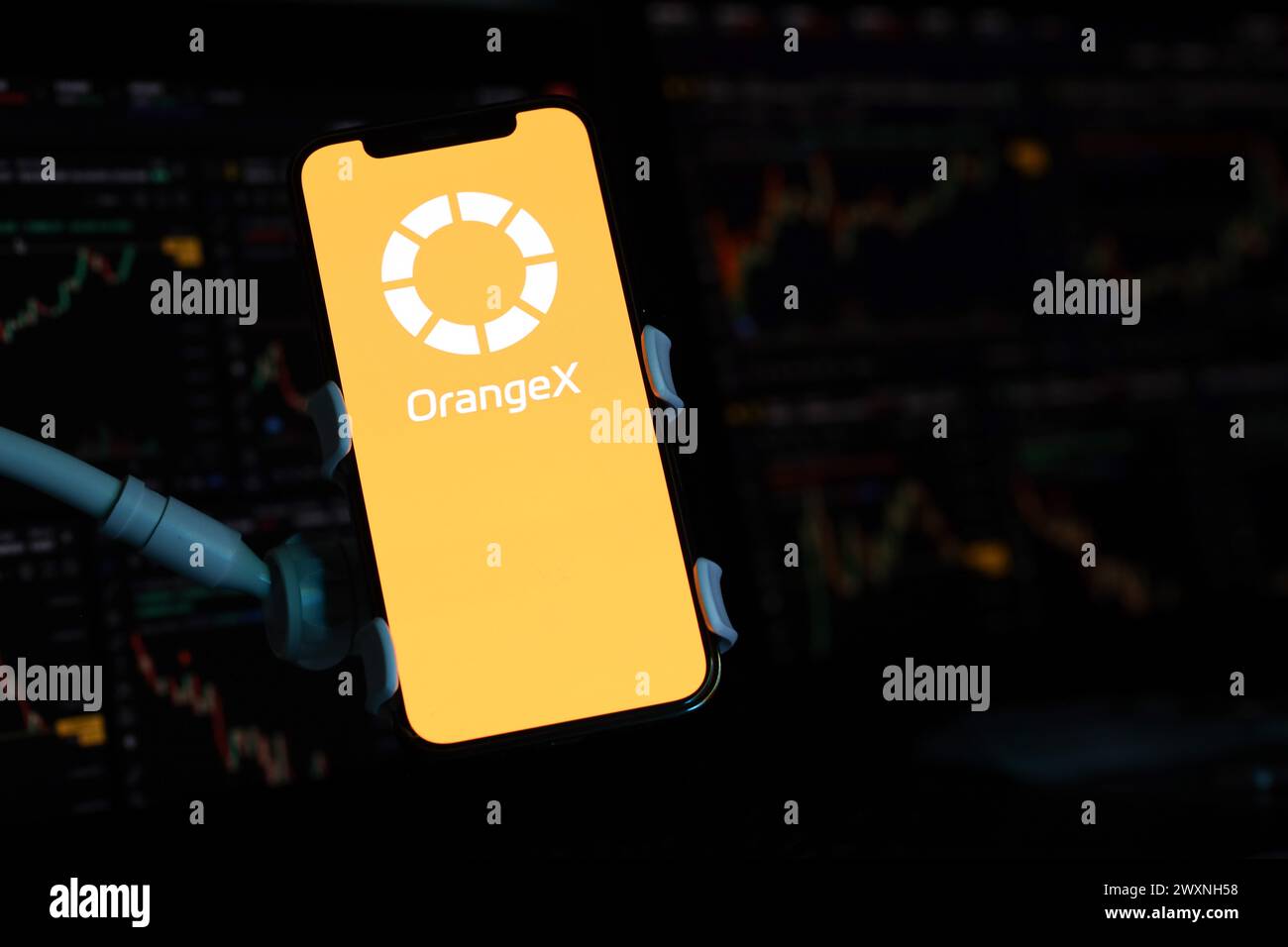 KYIV, UKRAINE - MARCH 15, 2024 OrangeX logo on iPhone display screen and crypto currency value charts. Cryptocurrency exchange portal Stock Photo