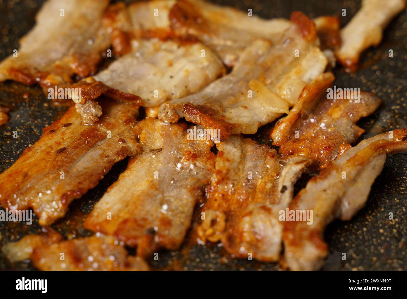 A detailed view of raw meat sizzling and searing on a hot cooking pan, with visible grill marks forming. Stock Photo