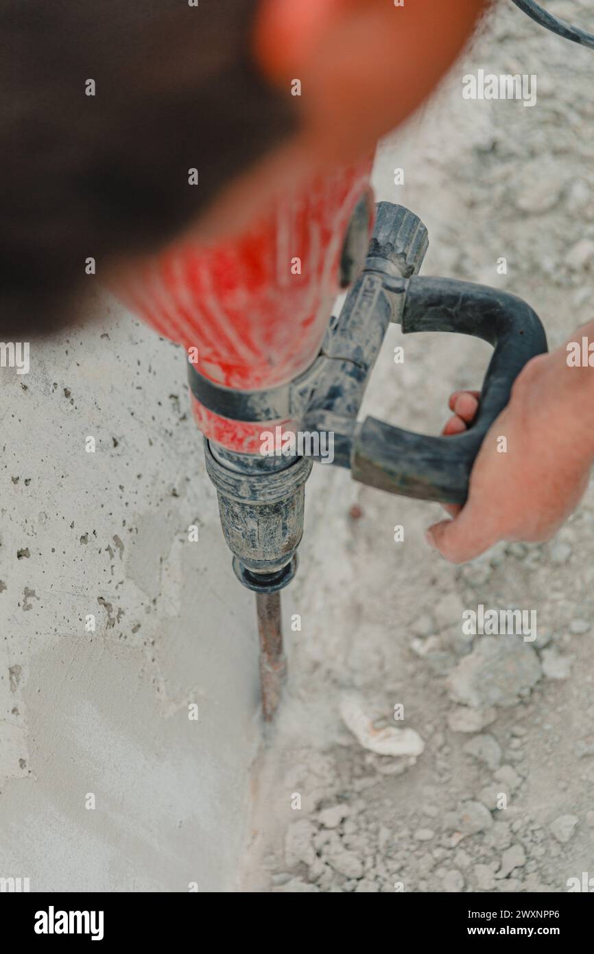 A man using a hand-held drill for concrete work on a sidewalk Stock Photo